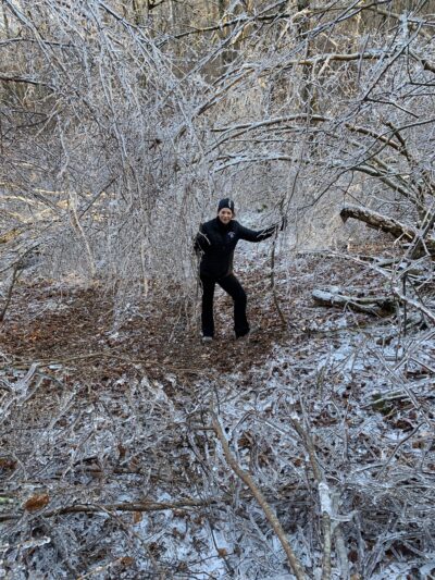 The author surrounded by ice-covered branches, holding two hiking sticks.