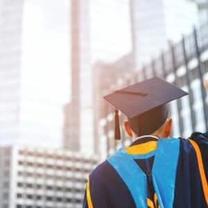 Back of a graduate wearing cap and gown looking up at city skyscrapers