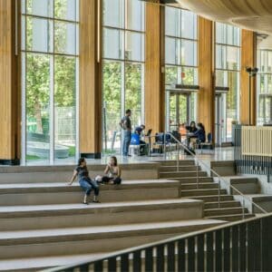 Indoor amphitheater with a wall of windows in the background and several college students hanging out on the top level