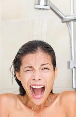 Image of white woman with brown hair from the shoulders up looking a the camera.  She is standing under a running shower, and she appears to be screaming.  Her mouth is wide open.  One eye is shut and the other is open.