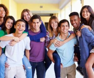 Group of teens looking at the camera, several carrying each other on their backs, piggy-back style.