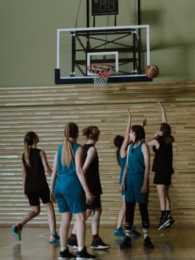 Teen girls playing basketball, all under the hoop after a shot has been taken.