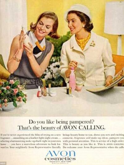 1950's style magazine ad for Avon cosmetcs.  Two women smiling as one holds up a perfume bottle for the other to admire. 
