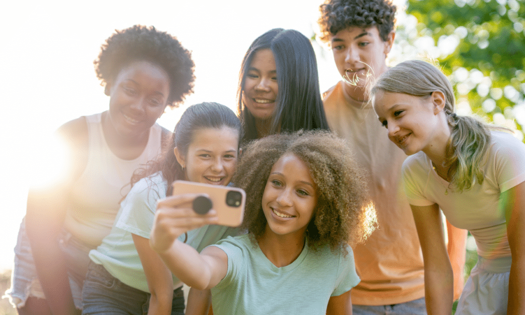 6 teens gathered around a cell phone while the front teen takes a group selfie