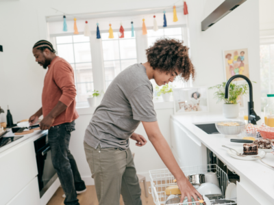 Teen boy unloading the dishwasher while his dad cooks at the stove in the background