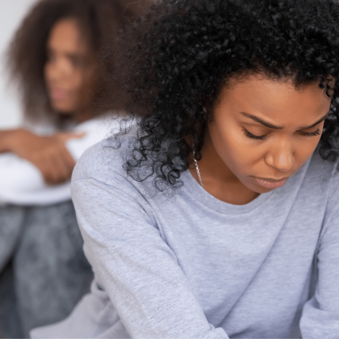 6 Mom looking looking upset with her head down close to the camera and with back to daughter. Teen daughter in the background with arms folded, not looking at Mom.