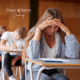 Teenage girl looking down at school work with concern in a classroom full of other students working.